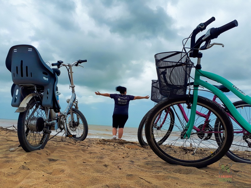 foto-mostra-pessoa-de-braços-abertos-entre-bicicletas-na-areia-da-praia-de-regência-linhares-es